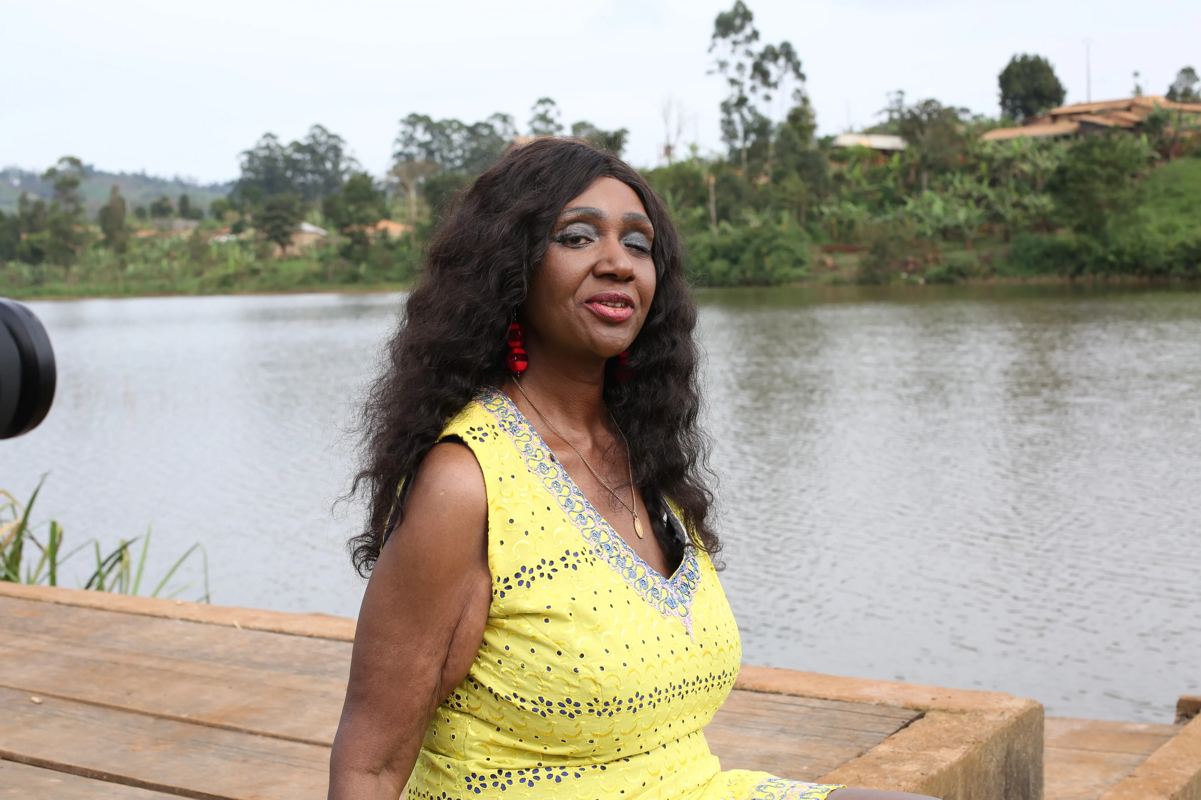 Angélina Tezanou en robe jaune et boucles d'oreilles rouges, au bord d'un lac dans l'ouest du Cameroun.
